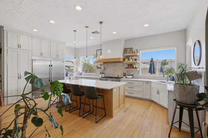 Gourmet kitchen featuring a large central island with seating, stainless steel appliances, extensive white cabinetry, light wood-finish flooring, and a patterned tile backsplash