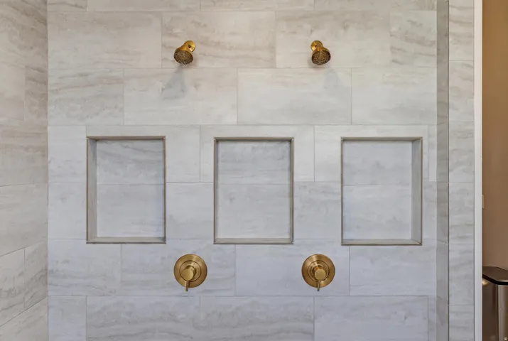 Shower surround featuring large-format tile, dual shower heads, and three recessed niches