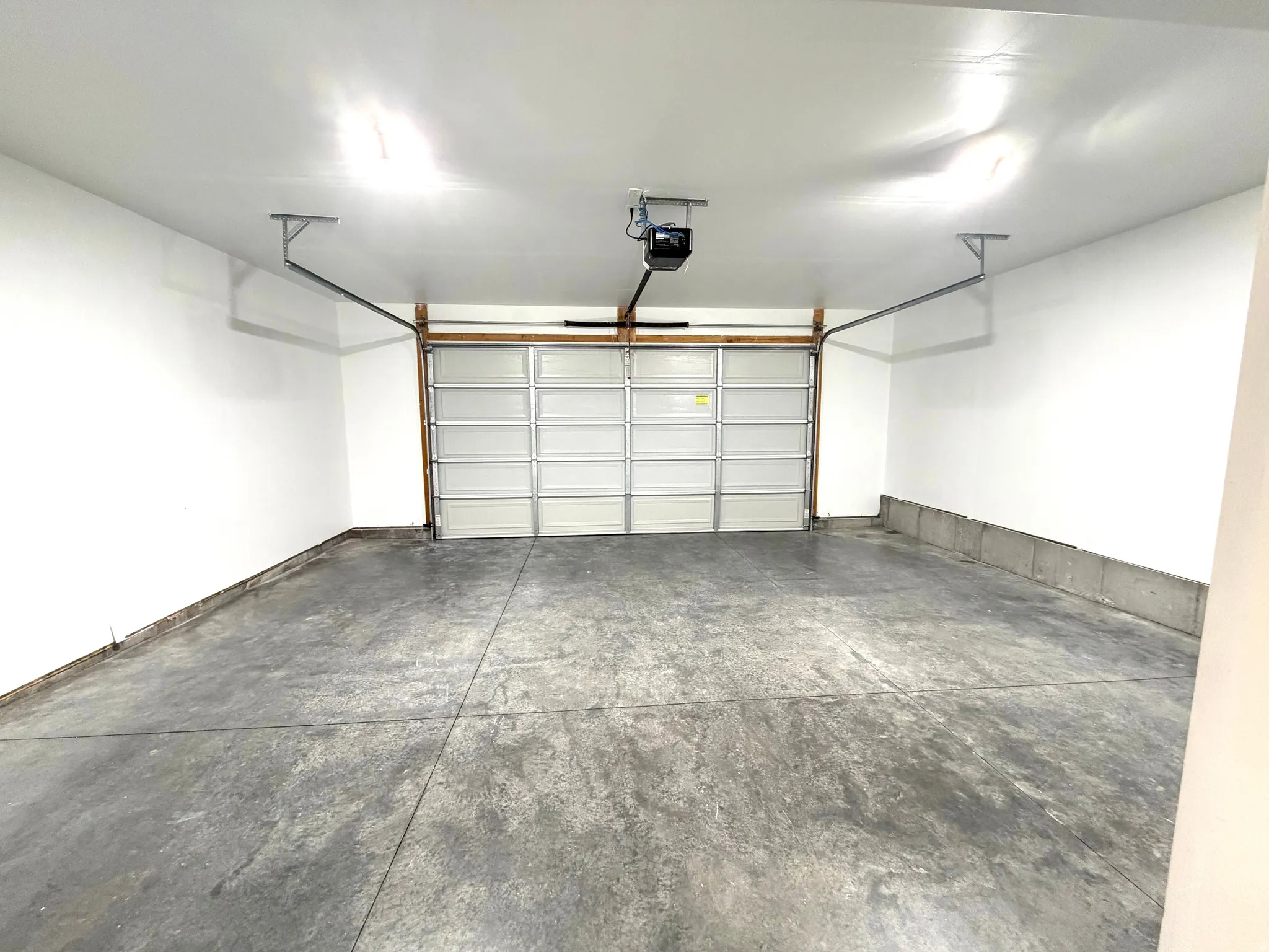 Concrete flooring, automatic garage door opener, white painted walls, overhead lighting