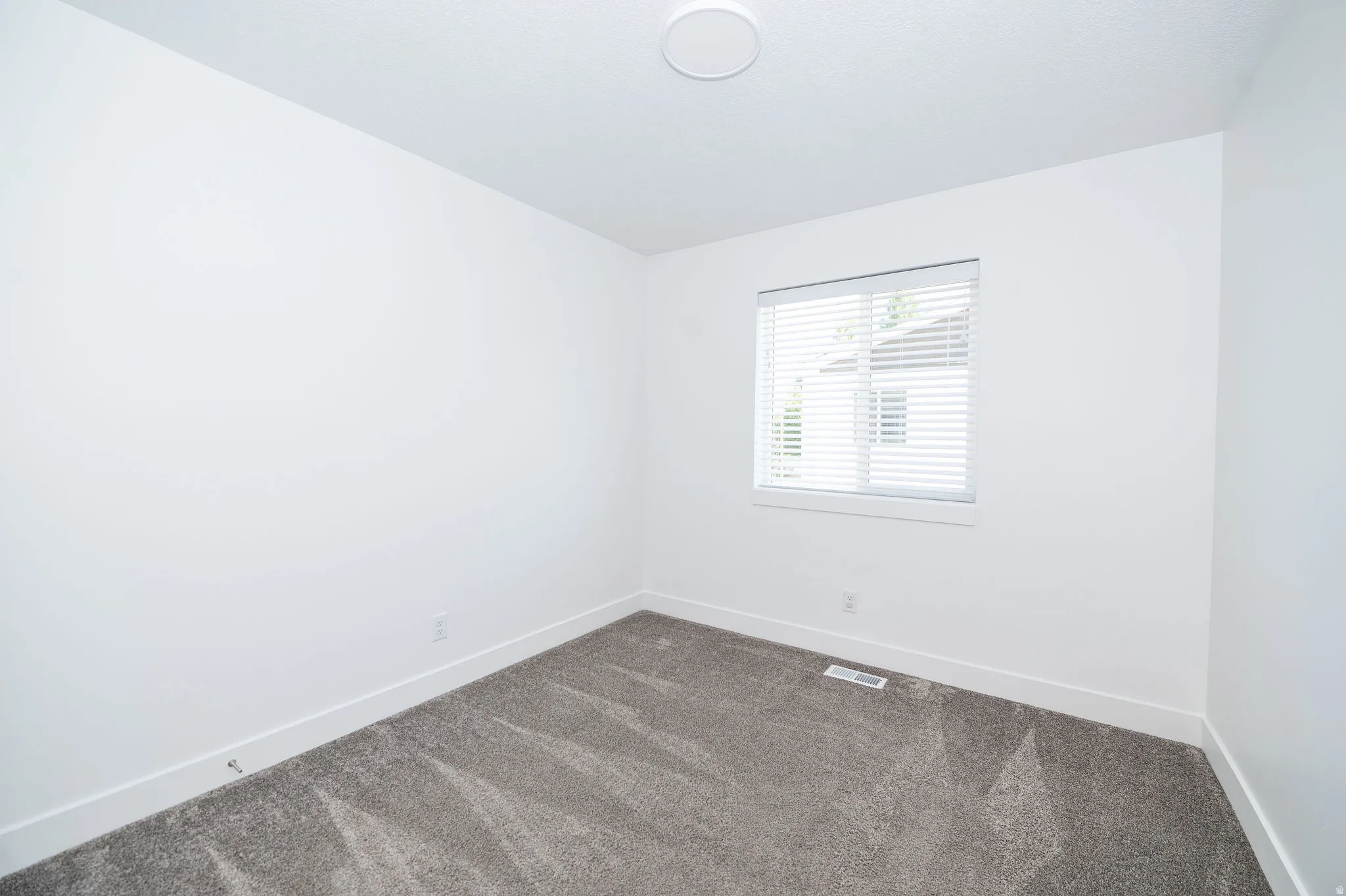 Room featuring grey carpeting, white baseboards, and a window with blinds