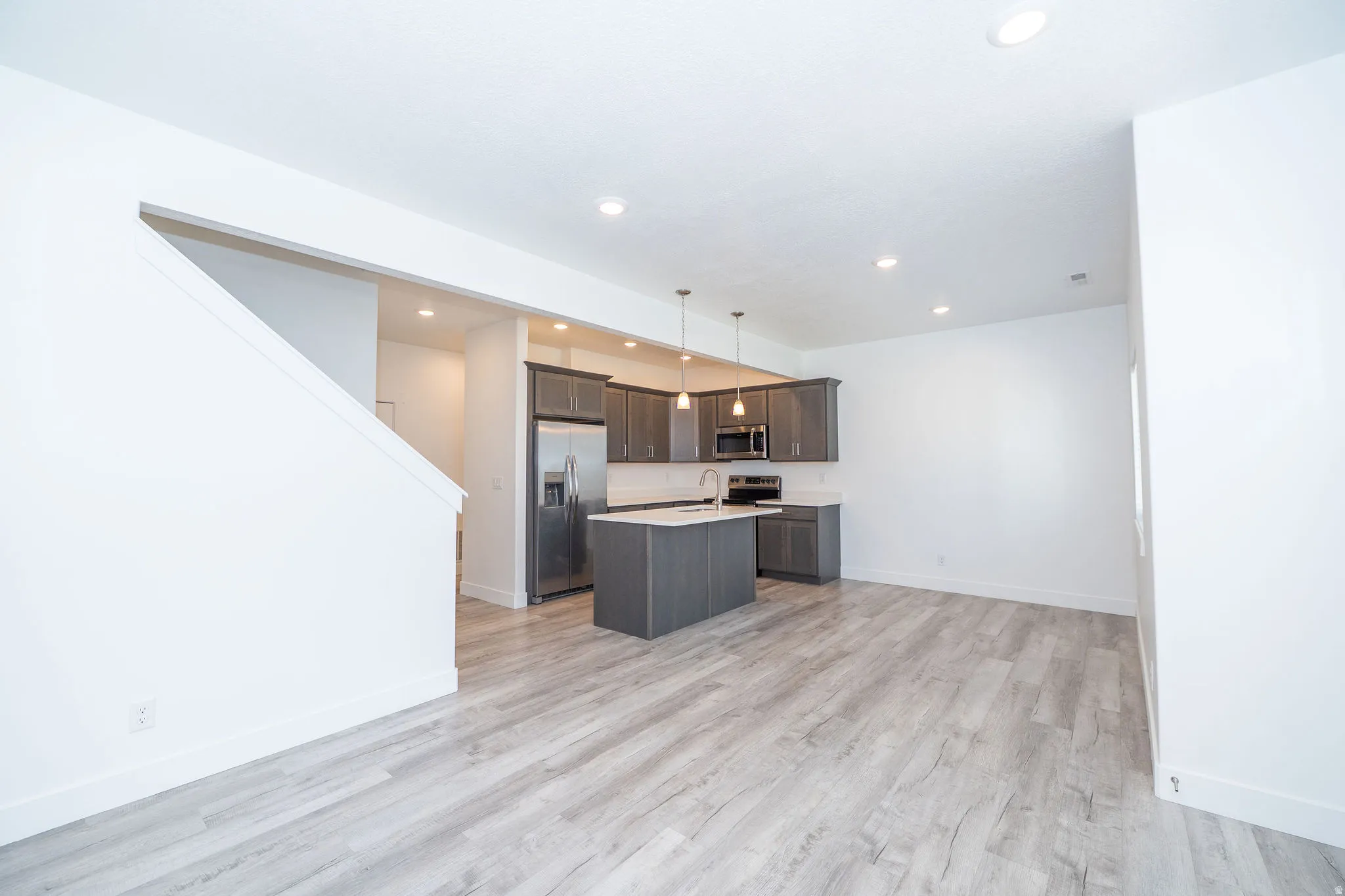 Open-concept living area featuring light wood-finish flooring, recessed lighting, and a contemporary kitchen