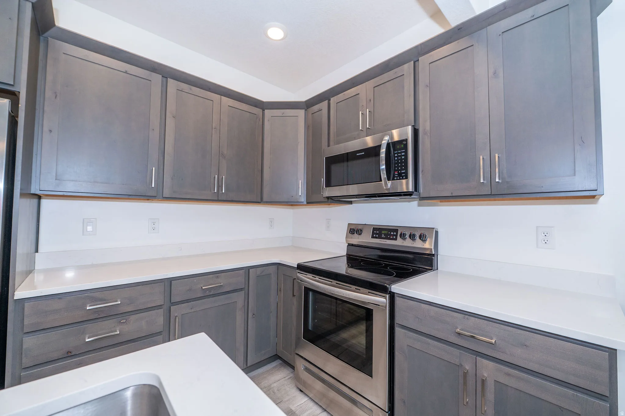 Kitchen featuring gray wood-finish cabinetry with silver hardware, light countertops, a stainless steel range, and a built-in microwave