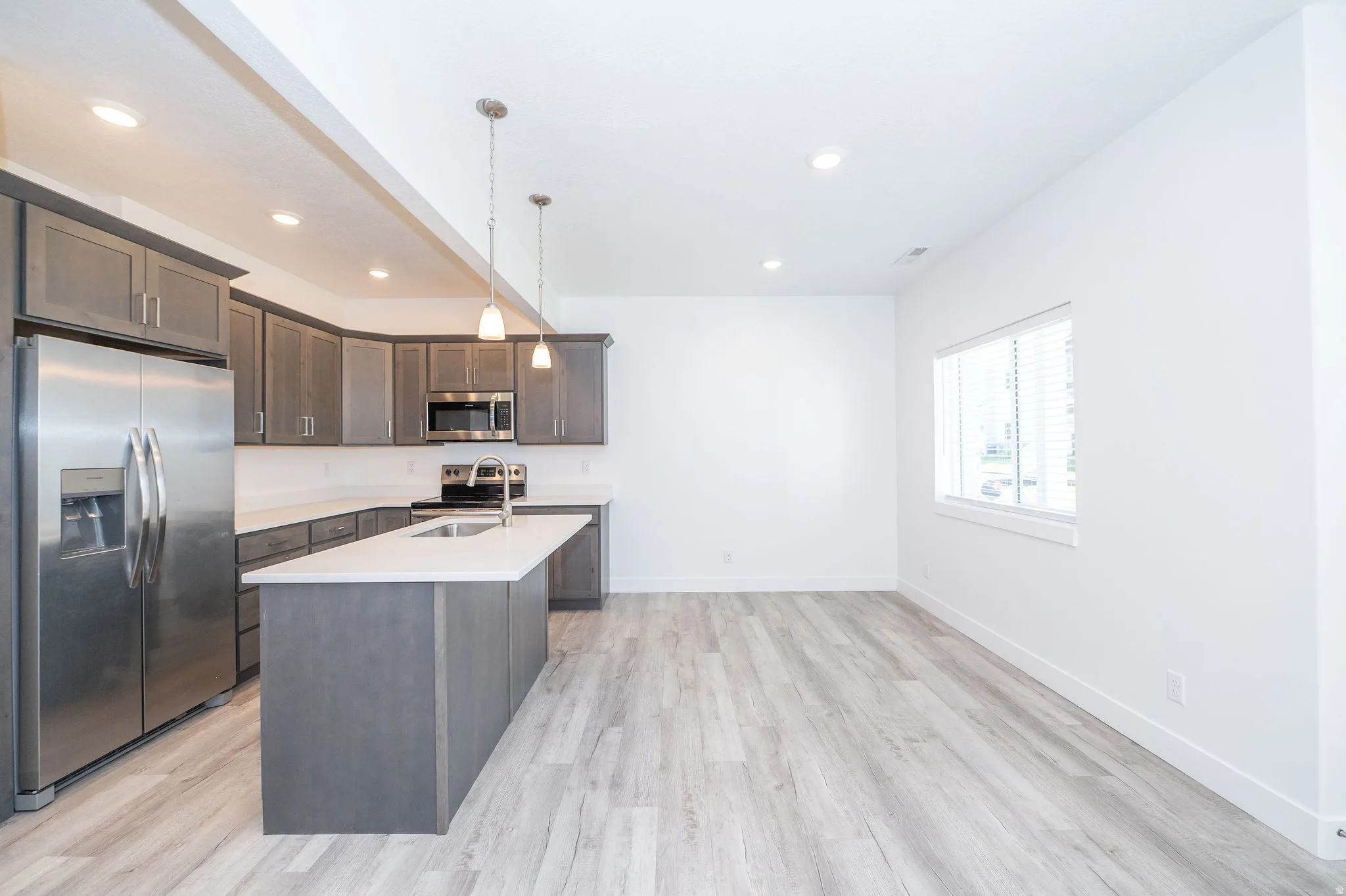Open-concept kitchen featuring gray cabinetry, stainless steel appliances, a central island with an undermount sink, pendant lighting, and wood-finish flooring
