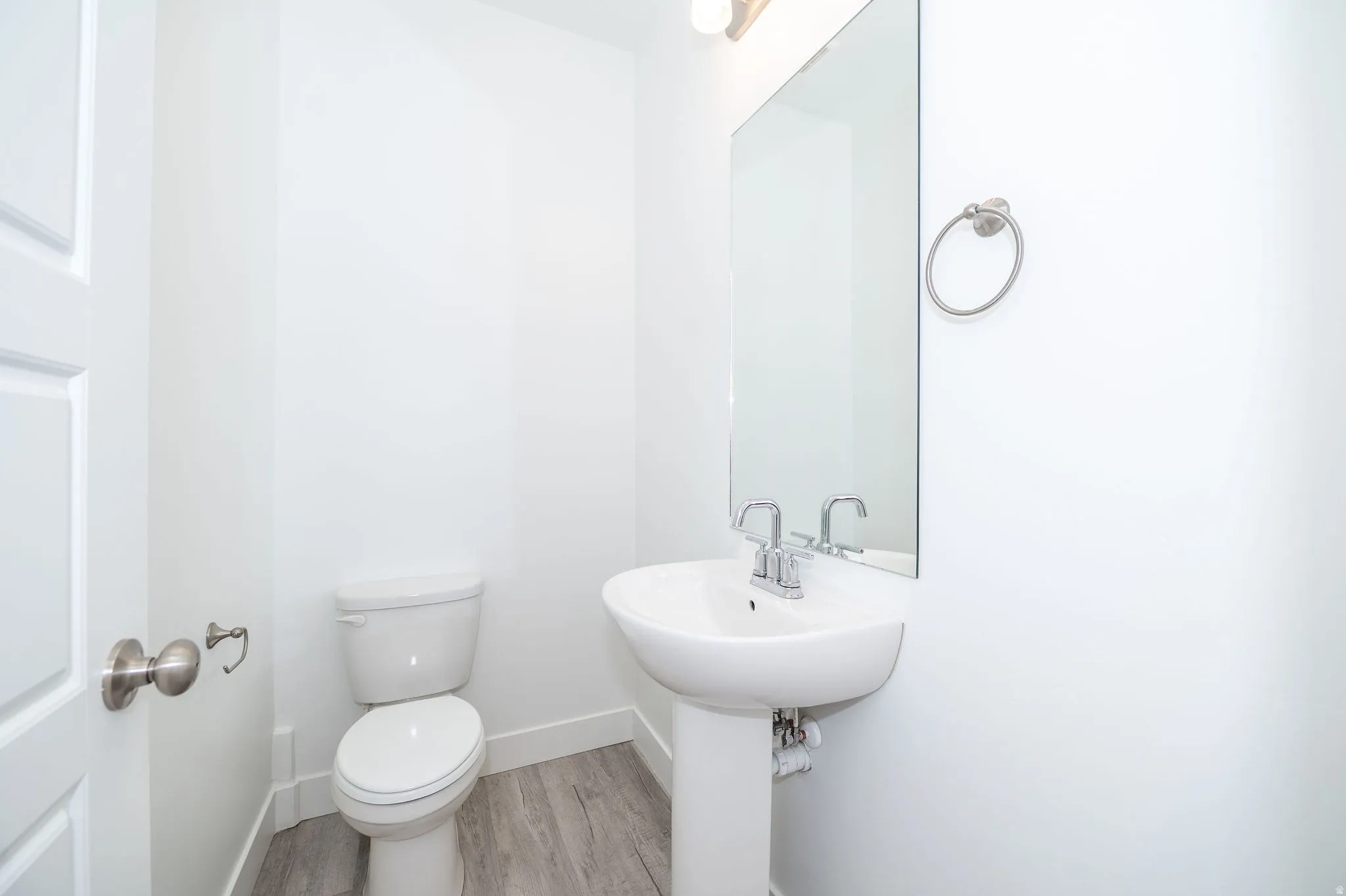 Powder room featuring a pedestal sink with chrome fixtures, a wall-mounted mirror, and wood-finish flooring