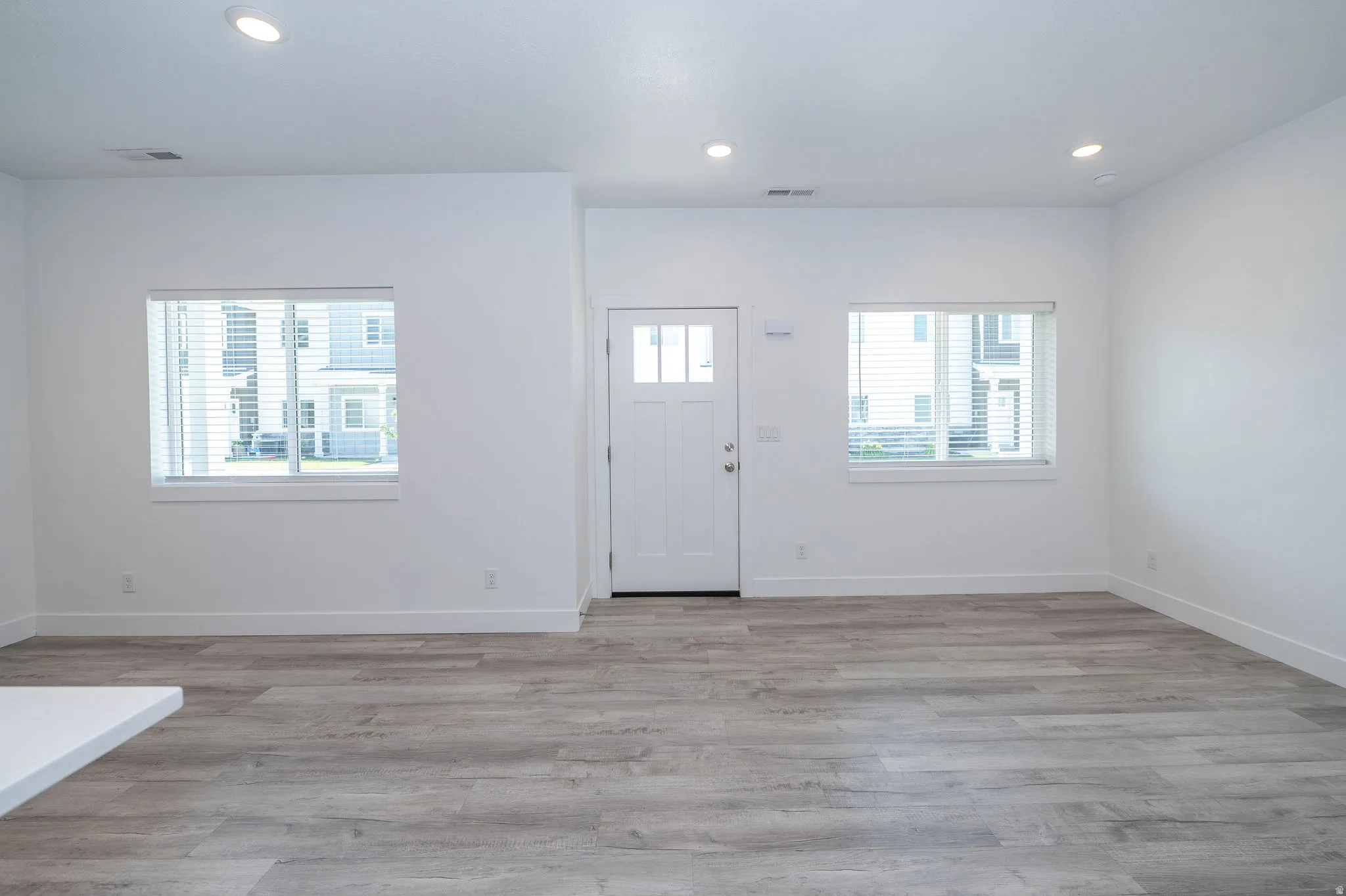 Entryway featuring a white paneled door with glass inserts, flanked by two windows with blinds