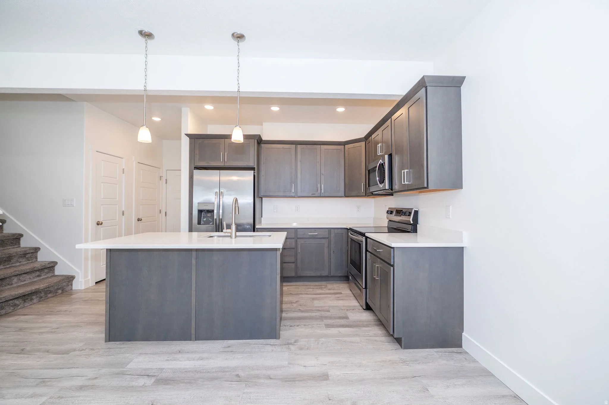 Kitchen featuring gray cabinetry, stainless steel appliances, white countertops, and a central island with an undermount sink