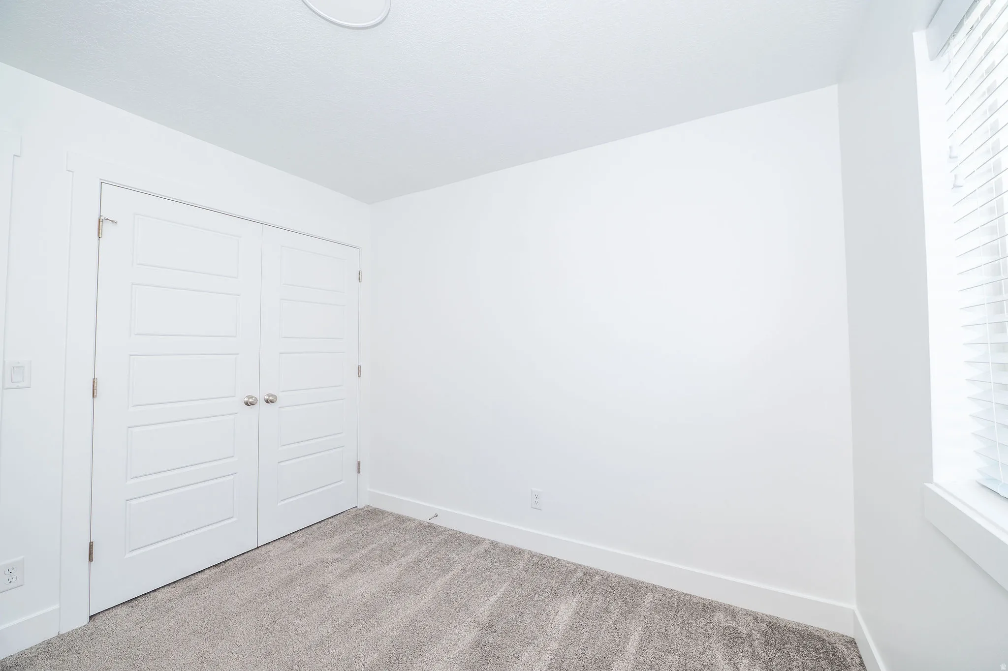 Carpeted interior space featuring white walls and a pair of white paneled bifold doors with chrome hardware