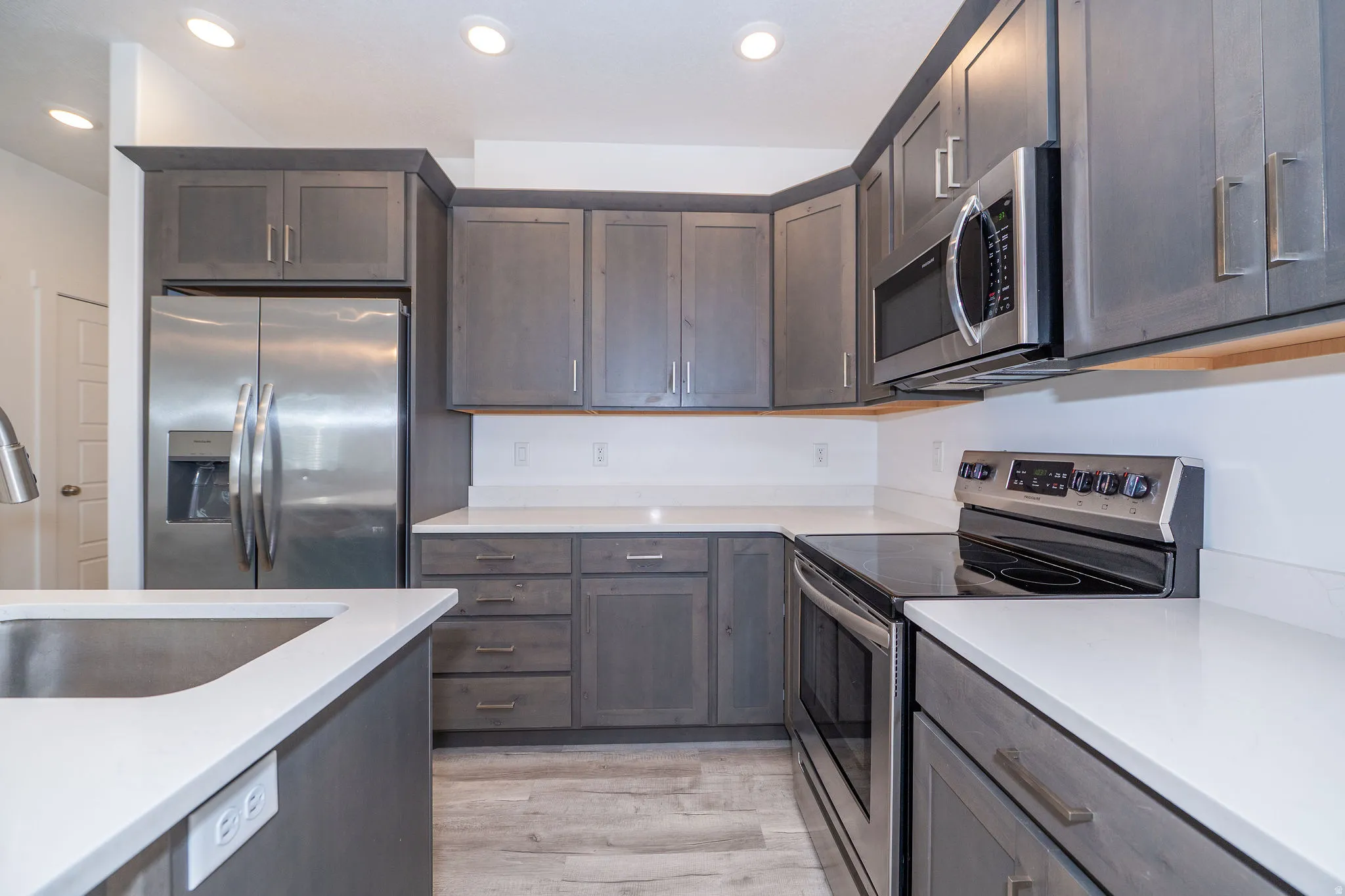Kitchen featuring dark wood-finish cabinetry, white solid surface countertops, stainless steel appliances, and recessed ceiling lighting