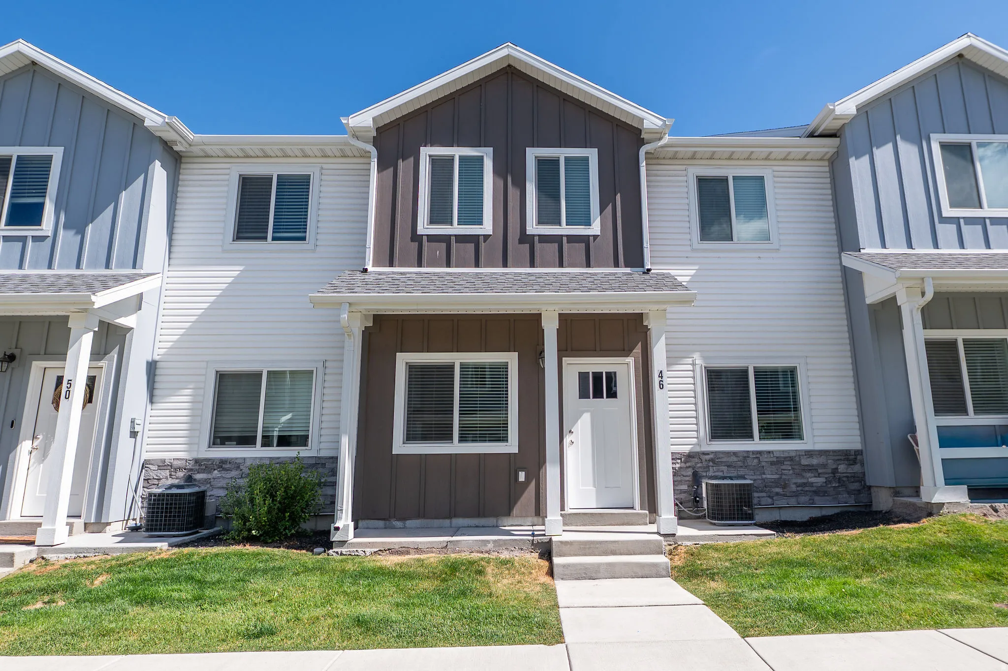 Two-story townhome with a white paneled facade and brown vertical siding
