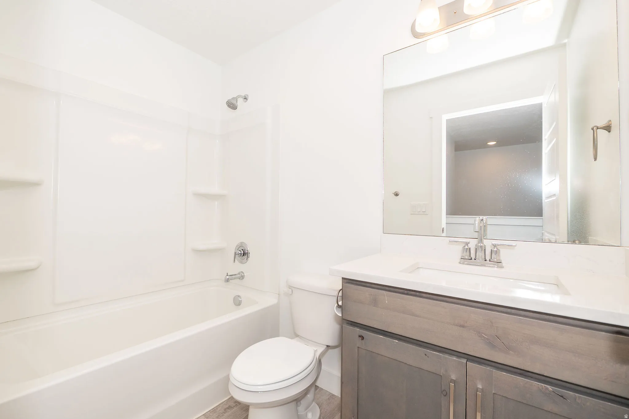 Full bathroom featuring a white tub and shower combination with integrated shelving, a sleek vanity with a light-toned countertop and an undermount sink, and wood-finish flooring