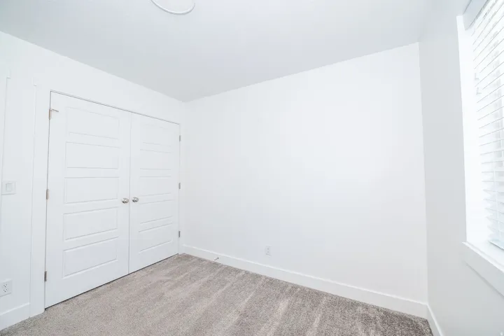 Carpeted interior space featuring white walls and a pair of white paneled bifold doors with chrome hardware