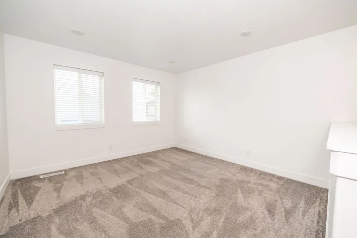 Spacious room featuring neutral carpeting, two windows with blinds, recessed lighting, and crisp white walls