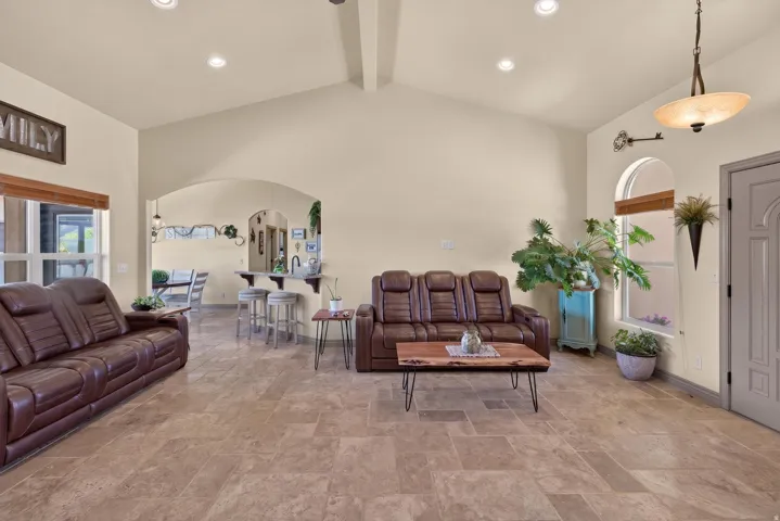 Spacious living area featuring neutral wall tones, tile flooring, and a vaulted ceiling with recessed lighting