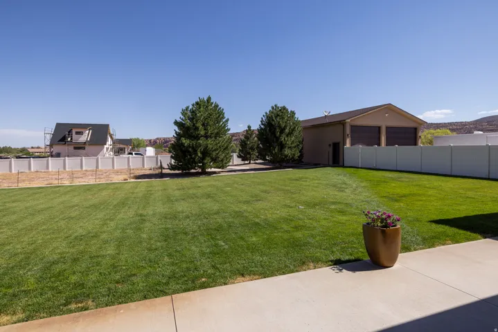 Expansive green lawn with mature evergreen trees, a concrete patio, and a detached two-car garage with roll-up doors