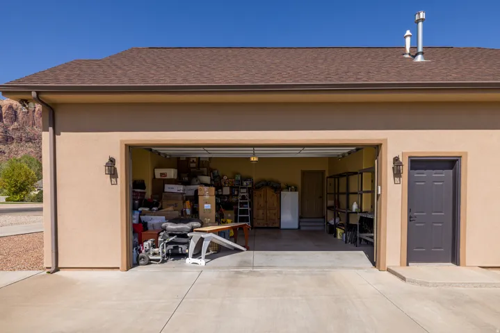 Attached garage featuring a light stucco exterior, brown shingle roof, and concrete driveway
