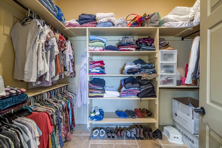 Custom closet system featuring multiple hanging rods, integrated shelving, and stone-finish flooring