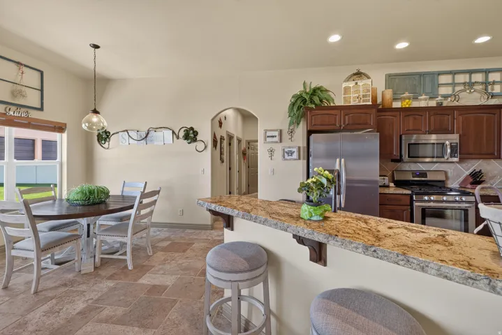Kitchen with a granite-top breakfast bar, stainless steel appliances, dark wood-finish cabinetry, and an arched doorway