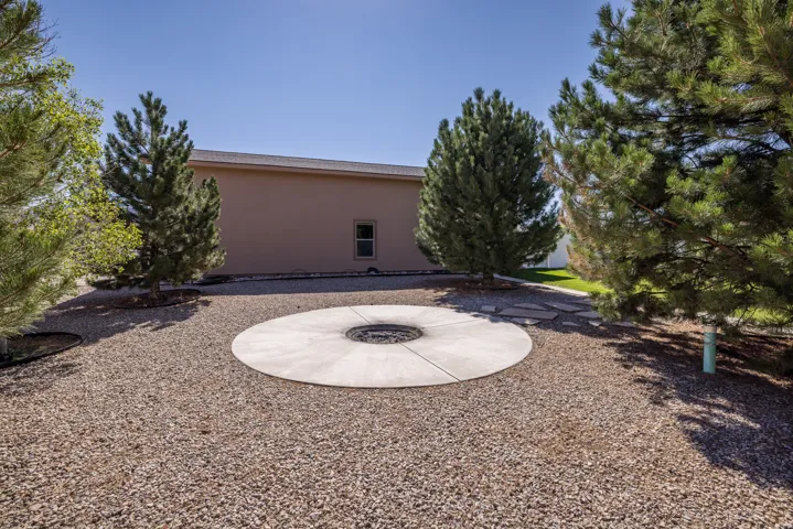 Gravel landscaping featuring a circular concrete patio with a built-in fire pit, surrounded by mature evergreen trees