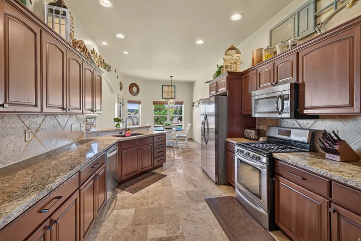 Spacious kitchen featuring warm wood cabinetry, stone countertops, a tiled backsplash, stainless steel appliances, and tile flooring
