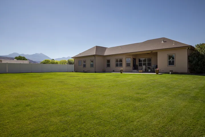 Expansive green lawn bordering a stucco exterior with multiple windows and a covered patio