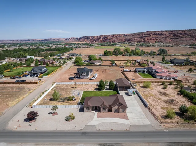 Expansive aerial perspective showcasing a residential property with a multi-car driveway, a detached garage structure, and a green lawn