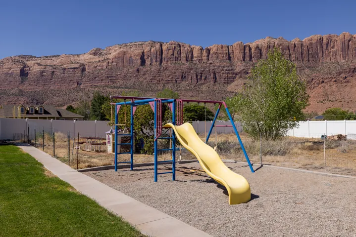 Outdoor play structure with a yellow slide and swings, set on a gravel base