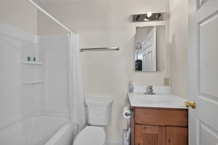Bathroom featuring a white tub and shower combination with integrated shelving, a white toilet, and a wood-finish vanity with a single basin sink