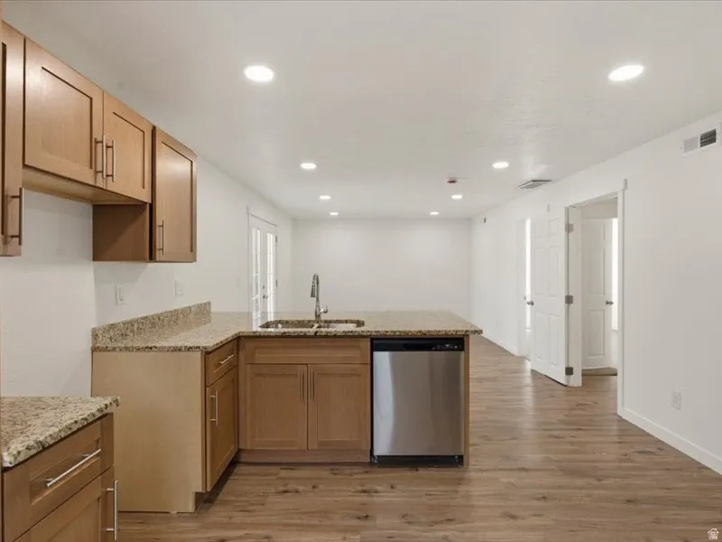Contemporary kitchen featuring light wood cabinetry, stone-finish countertops, and a stainless steel dishwasher