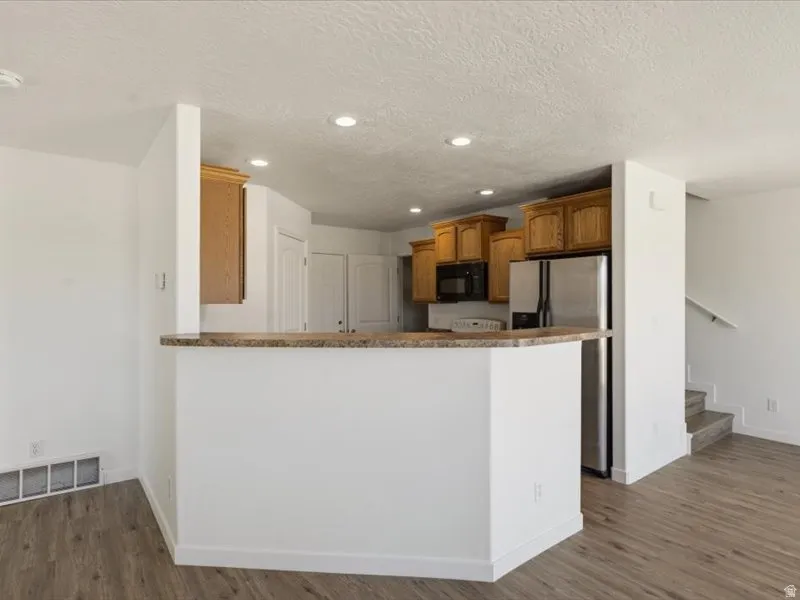 Kitchen area featuring a breakfast bar with a stone-finish countertop, wood-finish cabinetry, stainless steel appliances, recessed ceiling lighting, and wood-finish flooring