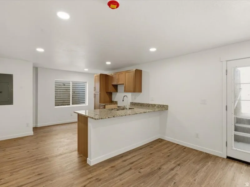 Open-concept living area featuring wood-finish flooring, recessed lighting, and a kitchen peninsula with a granite-style countertop