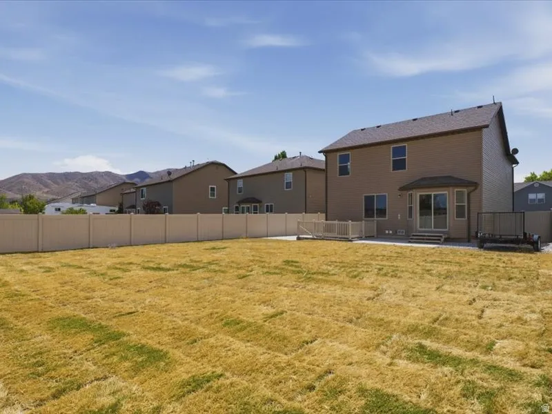 Expansive backyard featuring a privacy fence, concrete patio, and a wooden deck with railing