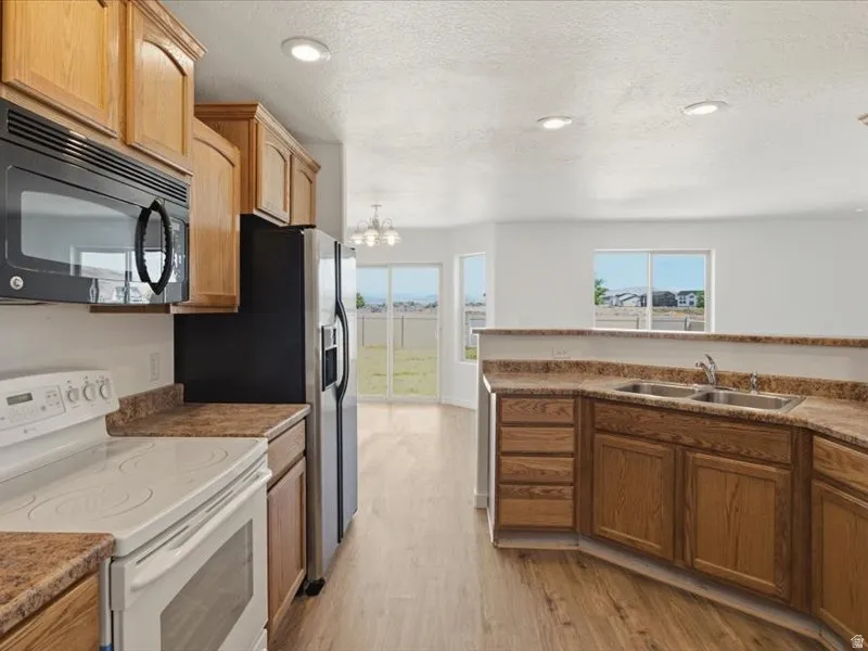 Kitchen featuring wood-finish cabinetry, a stainless steel refrigerator, a black built-in microwave, a white electric range, and laminate countertops