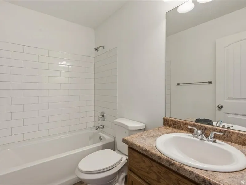 Full bathroom featuring a white subway tile tub surround, a white porcelain tub, and a vanity with a laminate countertop, an undermount sink, and chrome fixtures