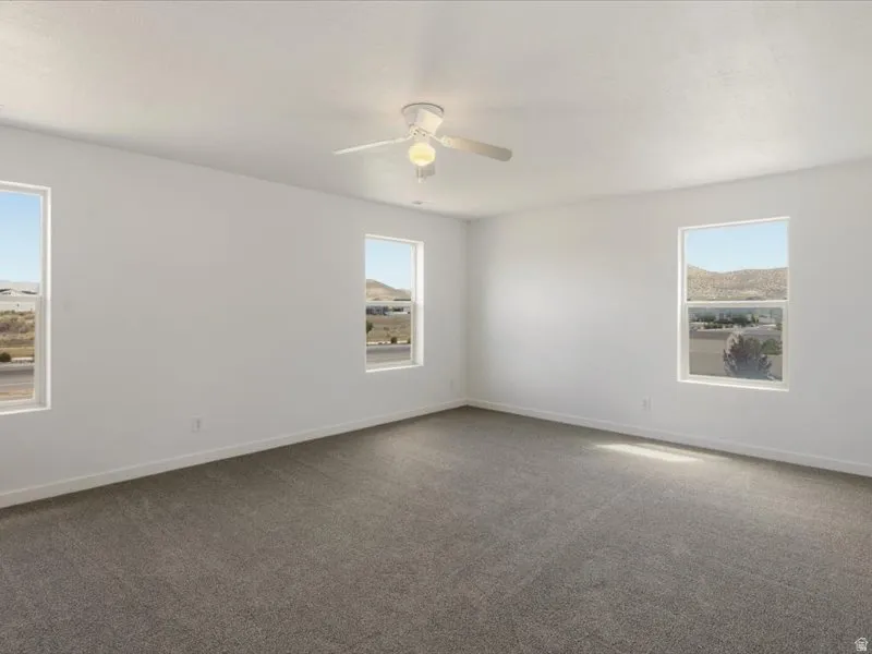 Spacious room featuring neutral carpeting, a ceiling fan with light fixture, and multiple windows providing natural illumination and mountain scenery