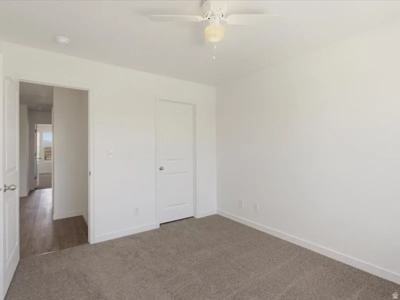 Carpeted room with white walls, a ceiling fan, and white trim