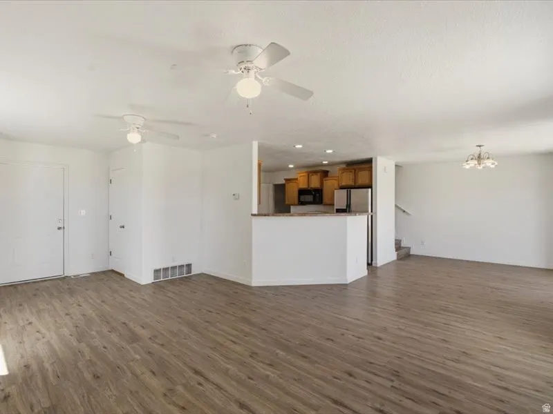 Expansive open-concept living area featuring wood-finish flooring, two ceiling fans, and a kitchen bar with a granite-look countertop