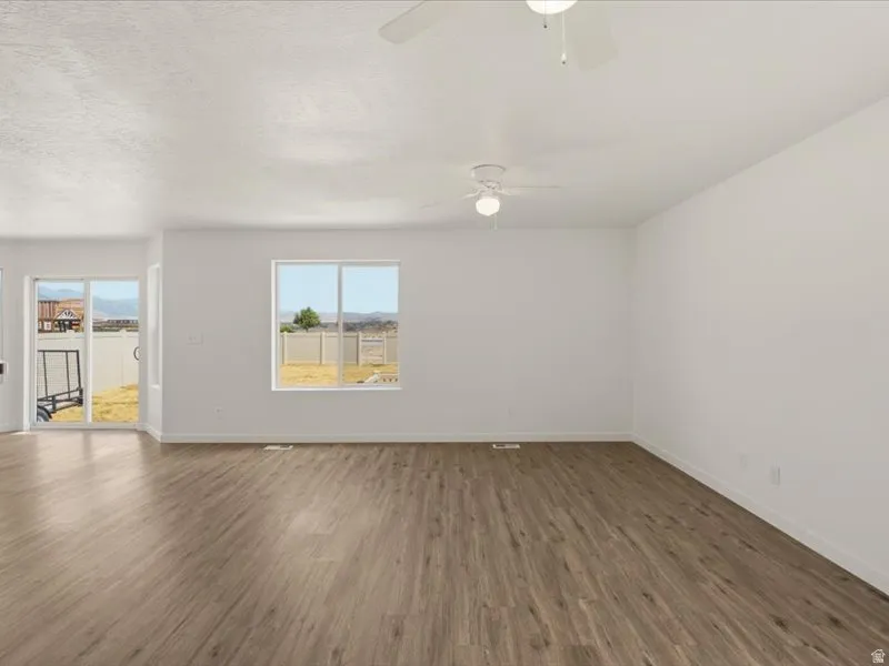 Spacious living area featuring wood-finish flooring, white walls, and multiple windows