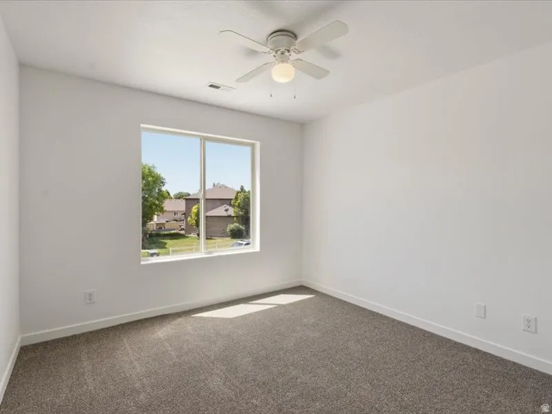 Room featuring a large window, neutral carpeting, white walls, and a ceiling fan with integrated lighting