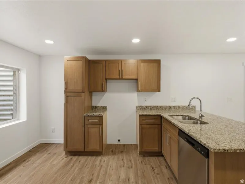 Kitchen featuring wood cabinetry, granite countertops, stainless steel sink with gooseneck faucet, and wood-finish flooring