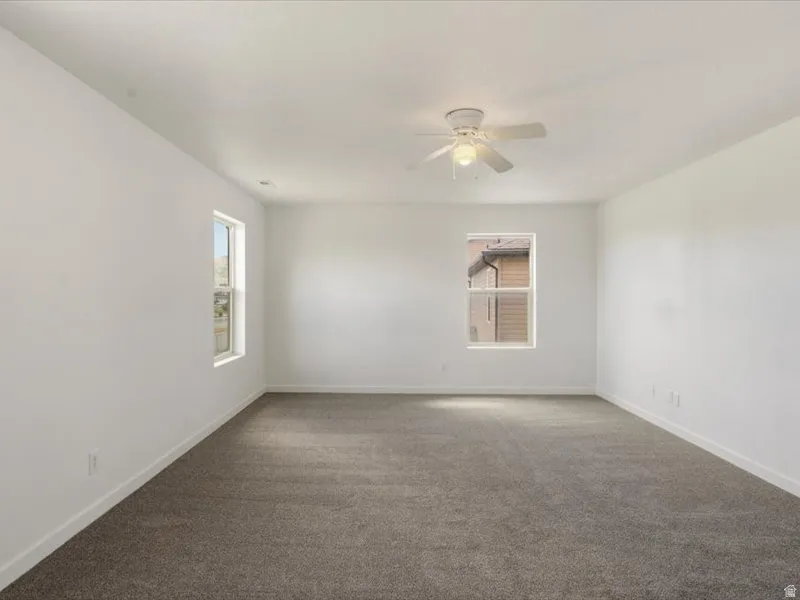 Spacious room featuring neutral carpeting, white walls, and a ceiling fan