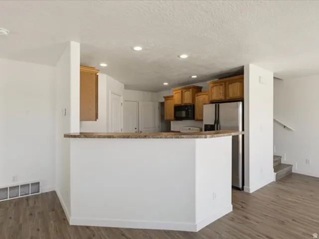 Kitchen area featuring a breakfast bar with a stone-finish countertop, wood-finish cabinetry, stainless steel appliances, recessed ceiling lighting, and wood-finish flooring
