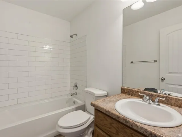 Full bathroom featuring a white subway tile tub surround, a white porcelain tub, and a vanity with a laminate countertop, an undermount sink, and chrome fixtures