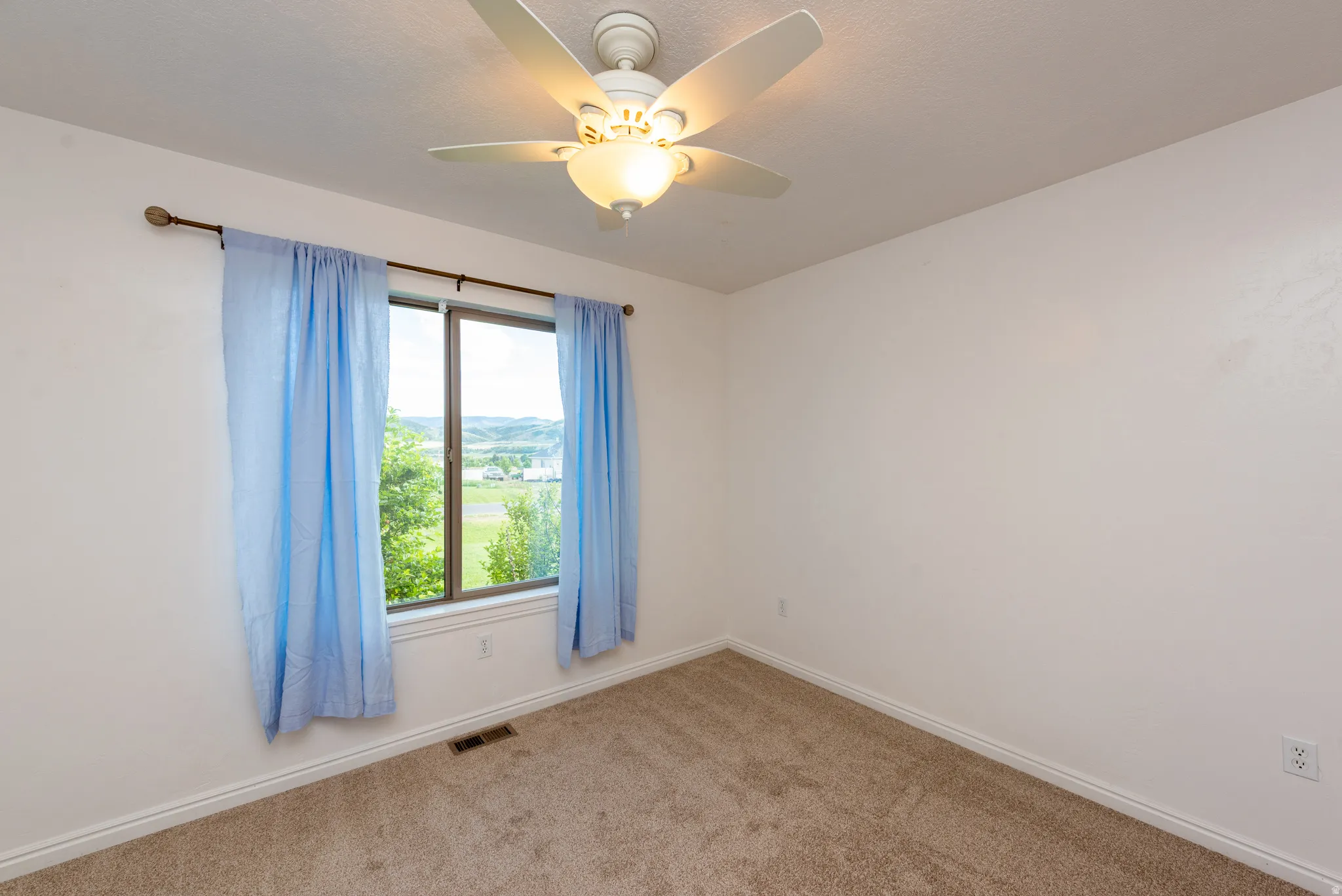 Bright room featuring a ceiling fan with integrated lighting, a window with exterior landscape, and neutral-toned carpeting