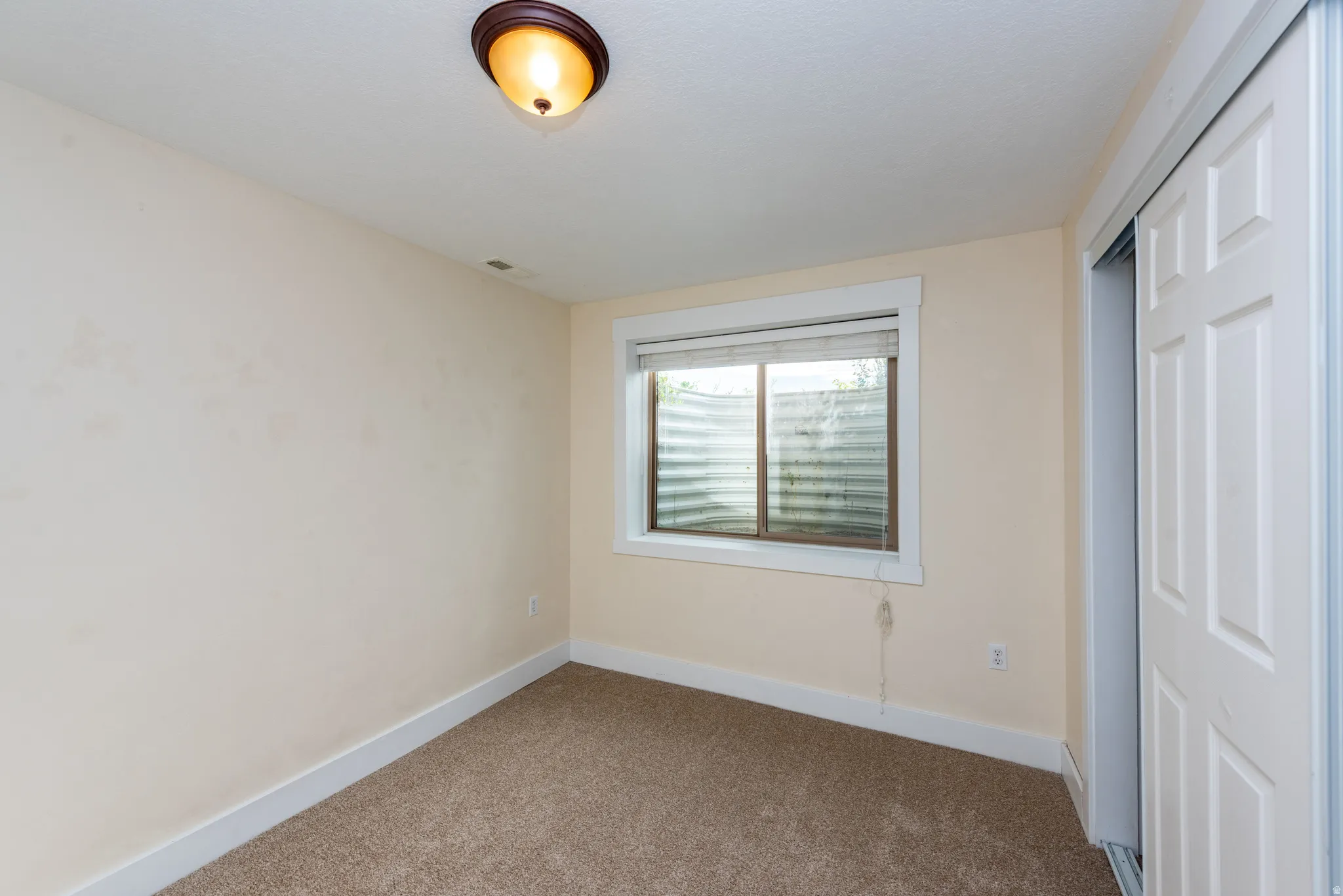 Carpeted room featuring a window, light-colored walls, white trim, and a sliding door closet