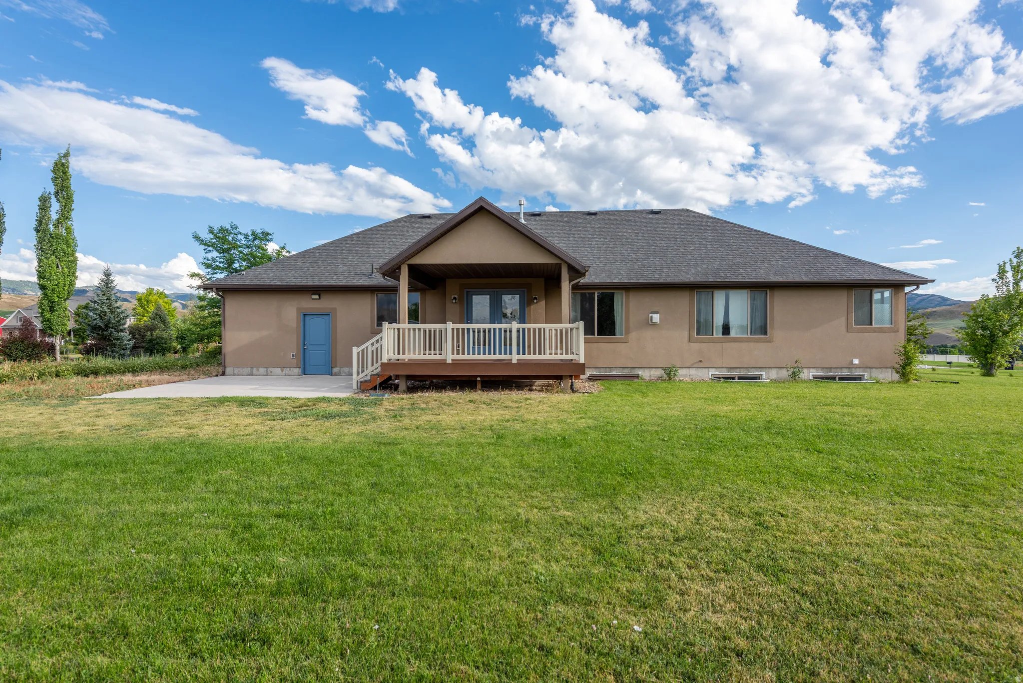 Spacious rear yard featuring a wide concrete patio and covered wooden deck with white railings