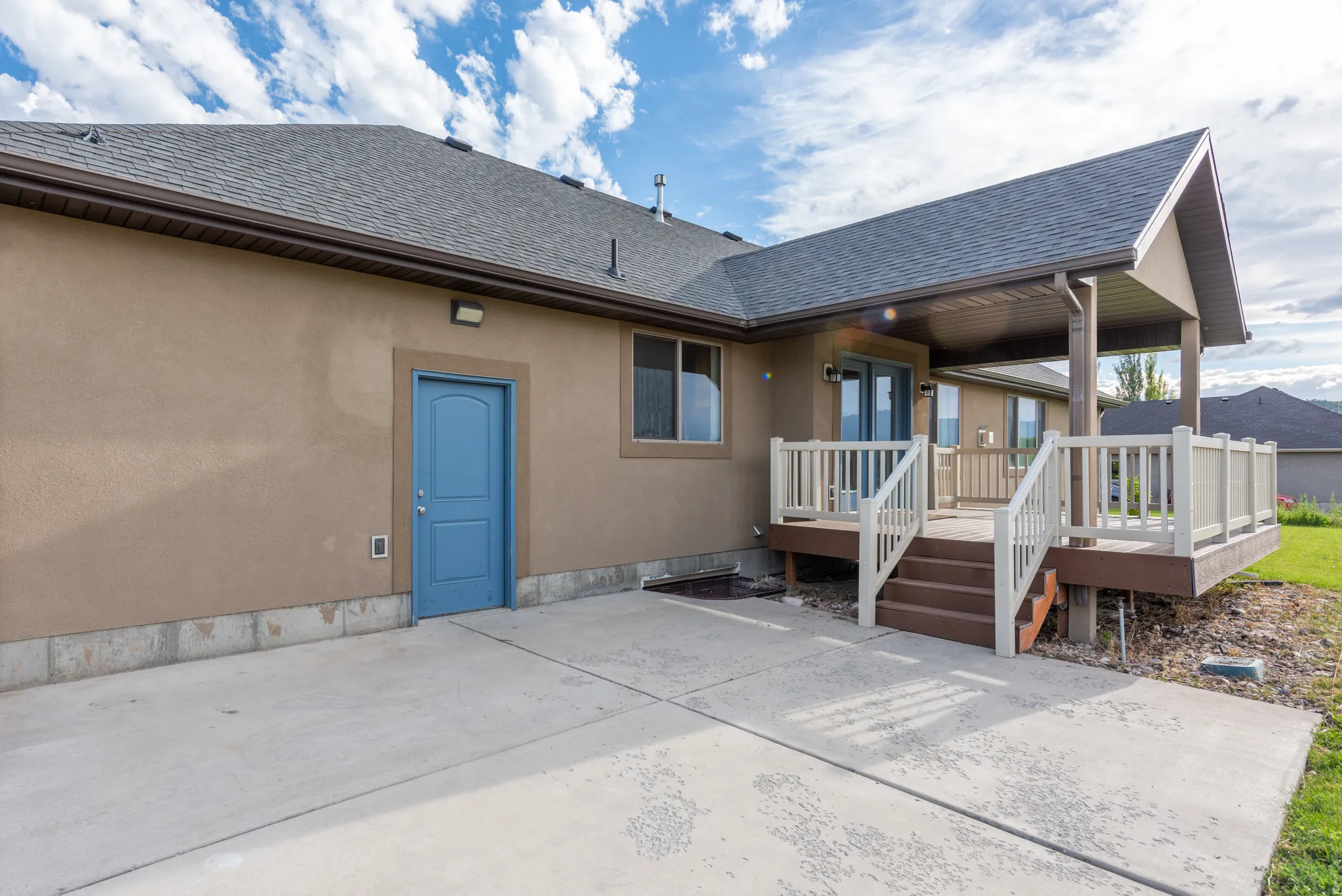 Stucco exterior featuring a covered deck, wood-finish railing, and a concrete patio