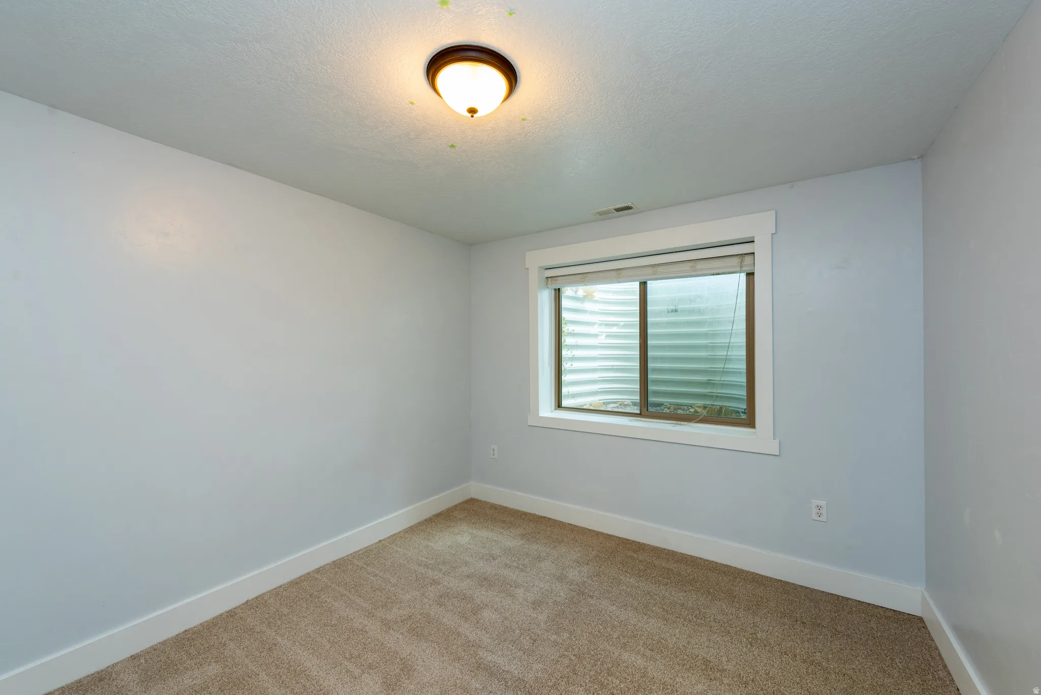 Carpeted room featuring a white window frame, a window well, a ceiling-mounted light fixture, and white baseboards