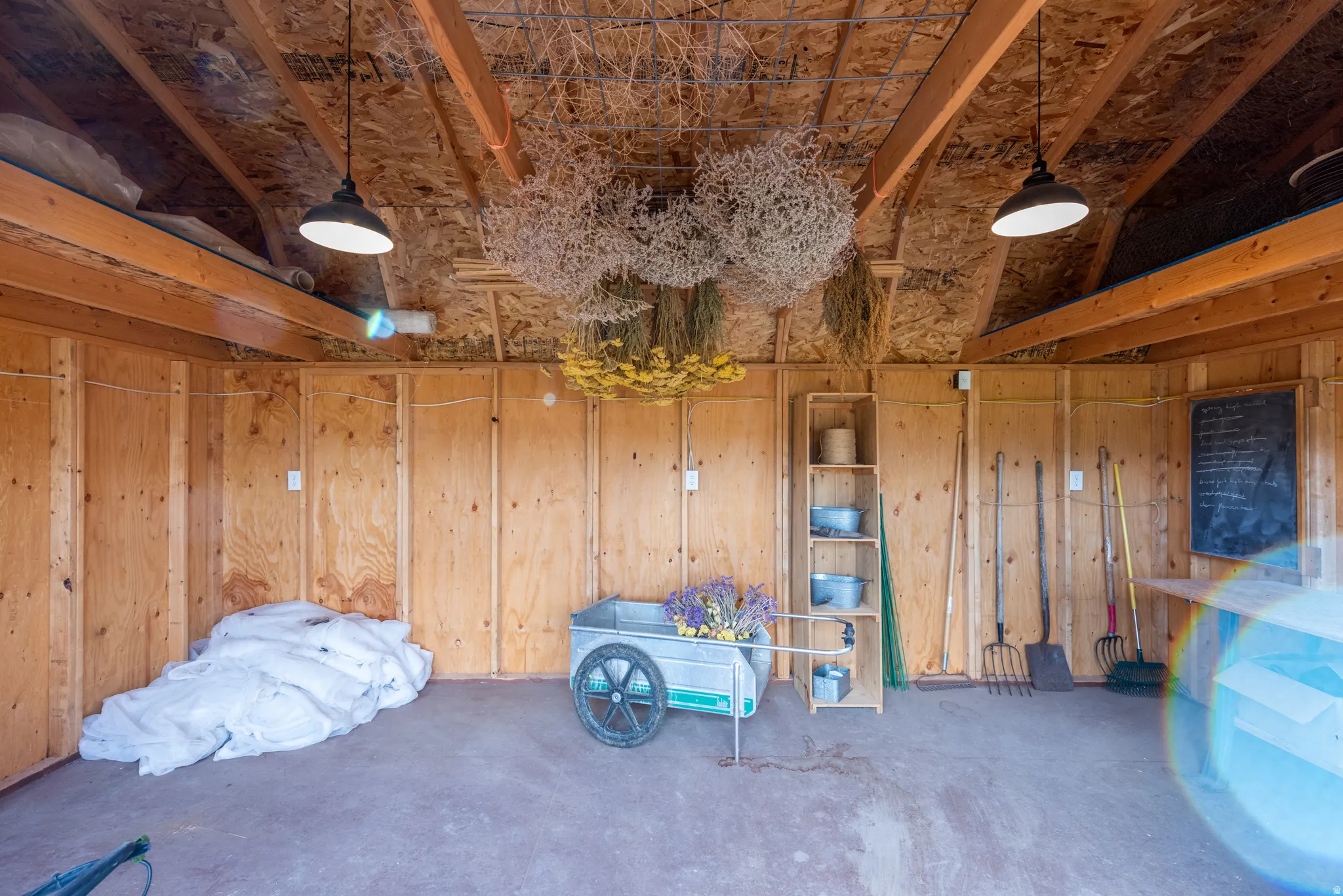 Spacious utility building featuring unfinished plywood walls, exposed rafter ceilings, concrete flooring, and overhead industrial lighting