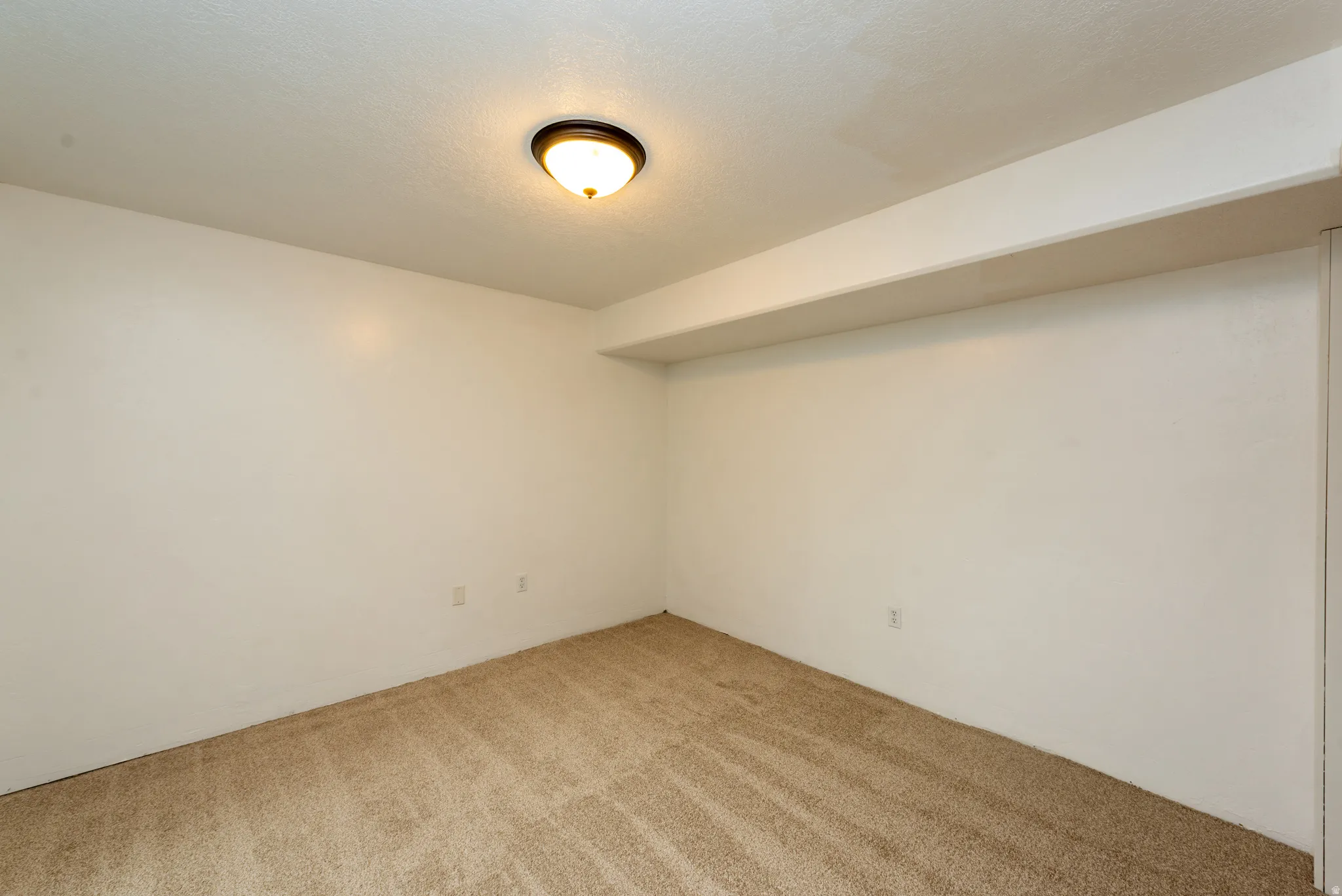 Carpeted room featuring a ceiling-mounted light fixture, white walls, and a visible ceiling beam