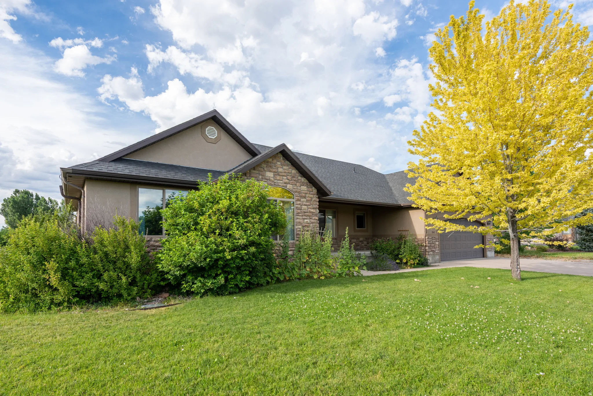 Split-level residence featuring stucco and stone veneer siding, an attached two-car garage, and a lush green lawn